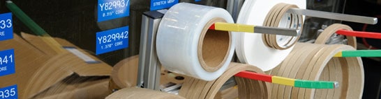 A roll of white tape with brown core and silver spool on a warehouse-style background.