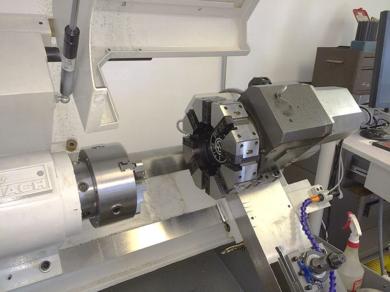 Large metal lathe with tool holders and attachments in a machine shop environment.