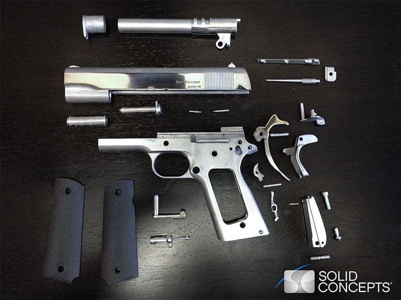 Disassembled 1911-style semi-automatic pistol with components laid out on a dark surface.