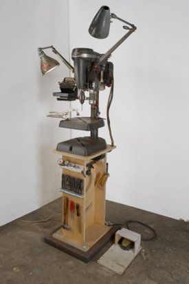 Vintage drill press station with wooden base, metal components, vice, and lamp.