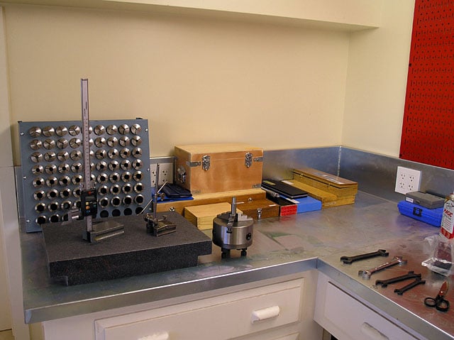 A metalworking bench with stainless steel top, multiple drawers, and various tools.