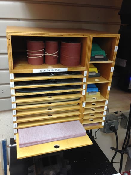 Wooden cabinet with shelves and drawers labeled "Drum Sander Rolls" in a workshop.