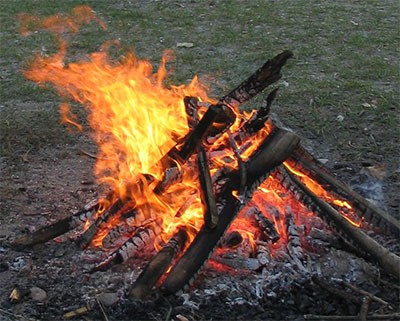 A campfire burning in an open field at night.