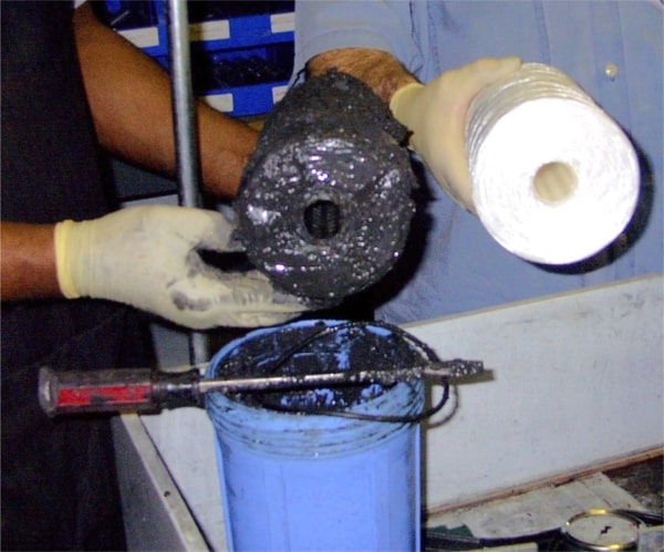 A person wearing white gloves holding a cylindrical object with black material covering it.