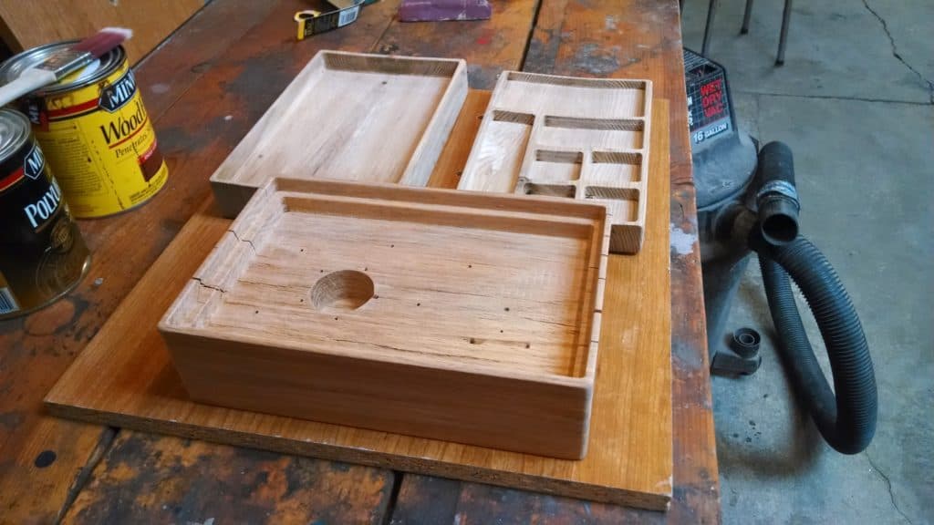 Unfinished wooden compartmentalized box on a workbench amidst woodworking tools and materials.