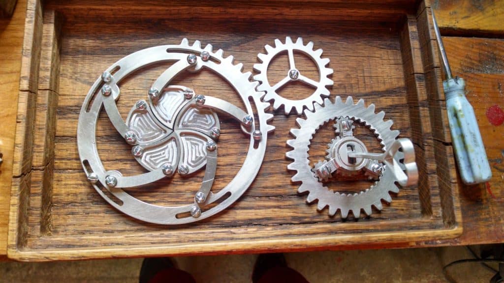 Silver metal gears in wooden box with screwdriver.