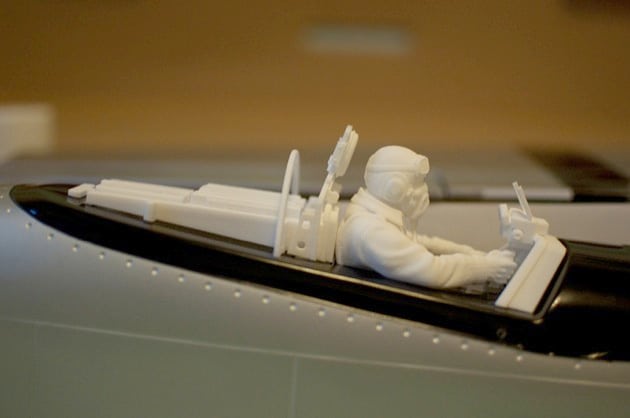 White plastic model of a pilot in an airplane cockpit with intricate controls and small pilot figure.