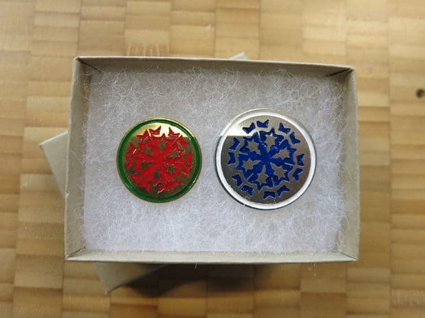 Two cloisonne enamel snowflake pendants in a decorative box.