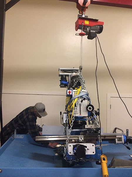 A man working at a metalworking machine suspended from the ceiling by a crane.