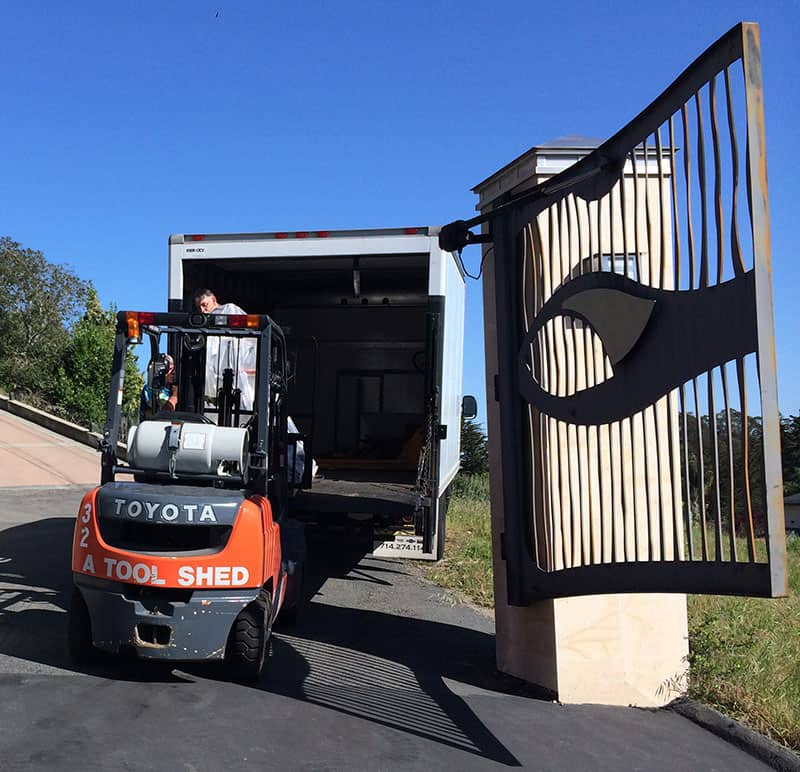 A forklift unloading a large truck from a secured facility with a distinctive gate design.