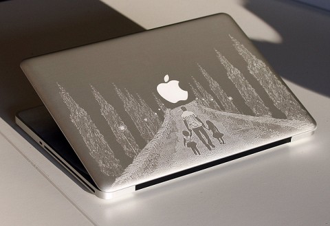 A silver MacBook with an intricately engraved forest design on its lid, featuring trees and a mountain peak.