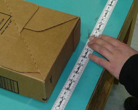 A person uses a ruler to measure a cardboard box on a teal table.
