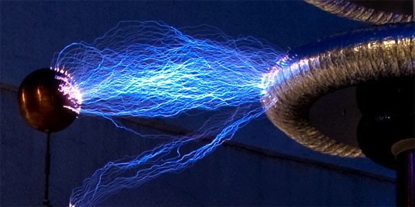 Tesla coil with bright blue sparks and dark background.