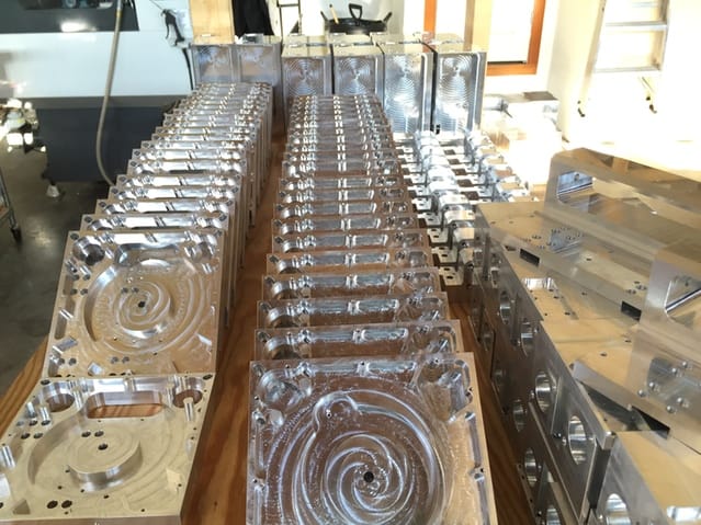 Precision-machined metal components with intricate designs and features, displayed on a wooden workbench.