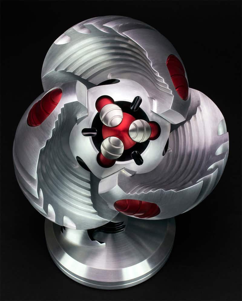 A silver and red metal object with a central hub, consisting of interconnected rings and protrusions, featuring a textured surface.
