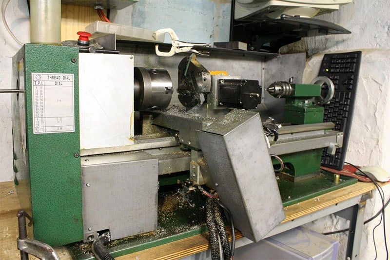 A green and gray lathe with a dial on the front in a machine shop setting.