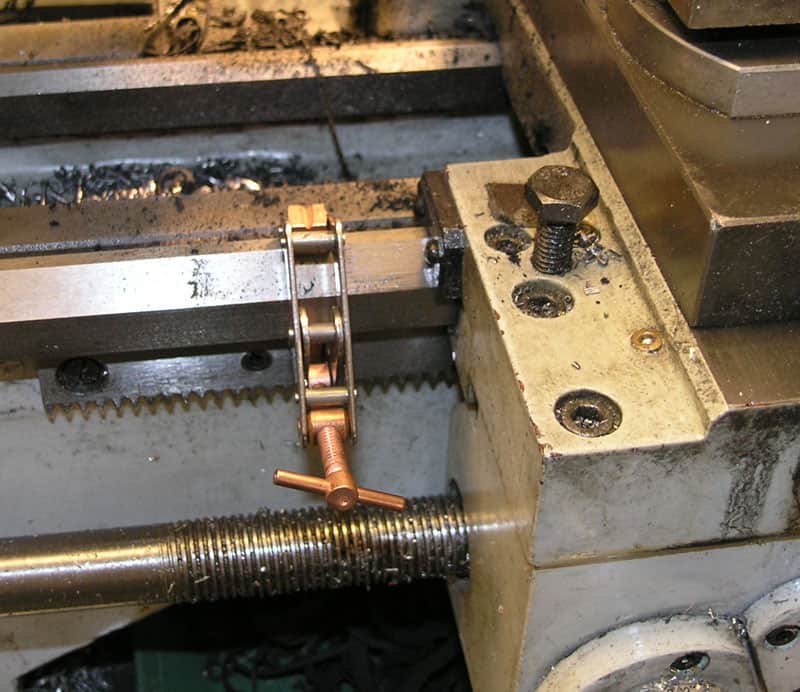 A close-up of a machine's metal components with a silver-colored serrated edge piece and copper-colored rod attached at an angle.