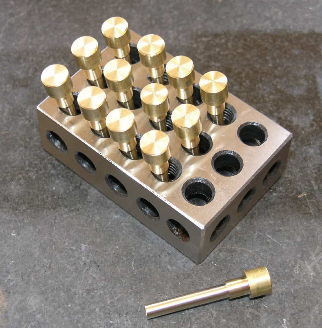 Metal block with brass dowel pins on a gray background.