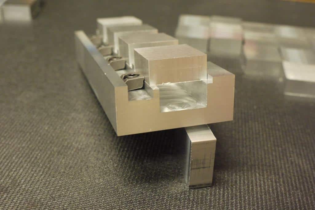 A metal vise block with small square holes and grooves on its top surface, used for holding or aligning objects.
