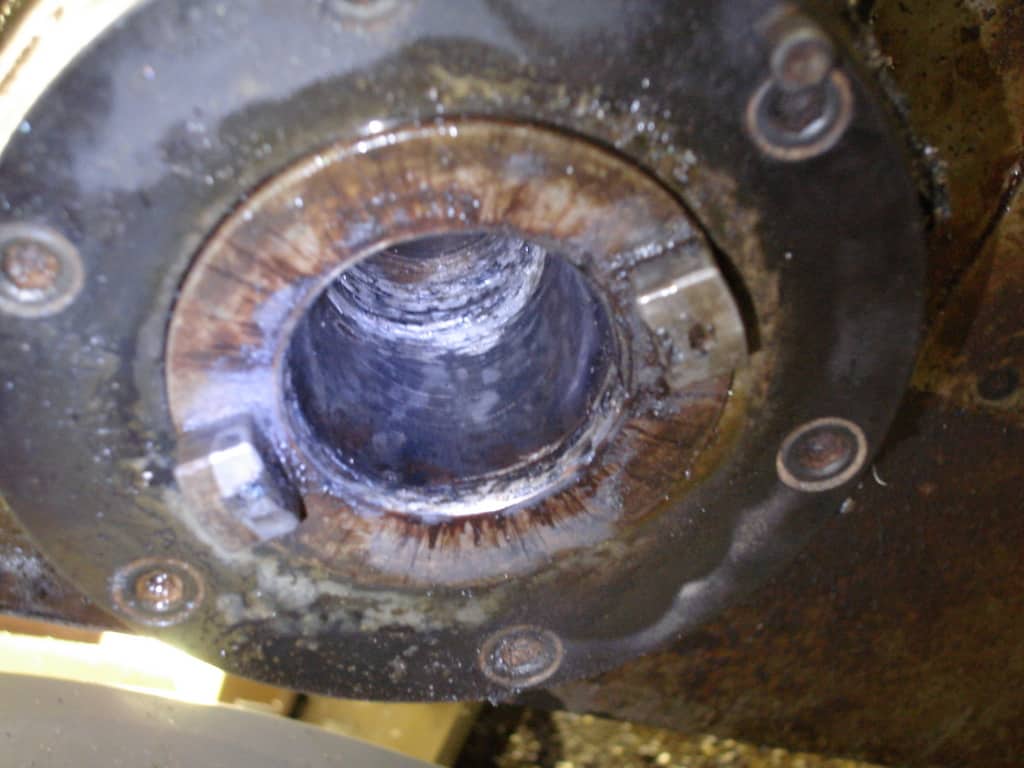 Close-up of dirty, rusty metal gear with large central hole and surrounding bolts.