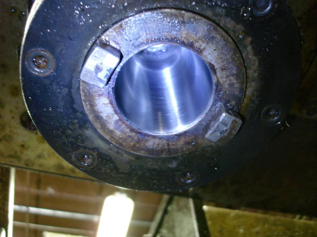 Metal component with circular opening, shiny silver surface, dark metal ring, rust, and corrosion.