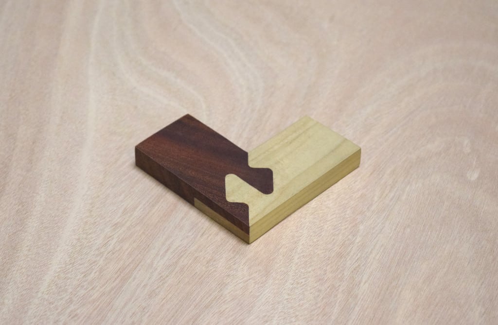 Dark brown and light-colored wood puzzle piece on light-colored wood background.