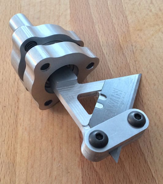 Triangular silver metal part with two holes containing small black ball bearings on a smooth aluminum surface.