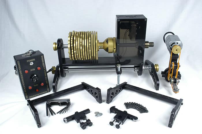 Black metal lathe with brass components and assorted accessories on a white background.