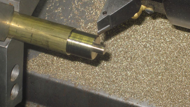 Close-up of a brass rod with machined end in a machine shop setting.