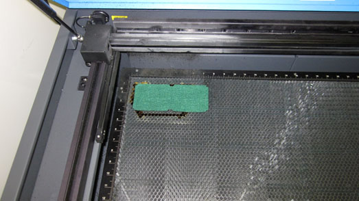 A laser cutter machine with a green felt pad.