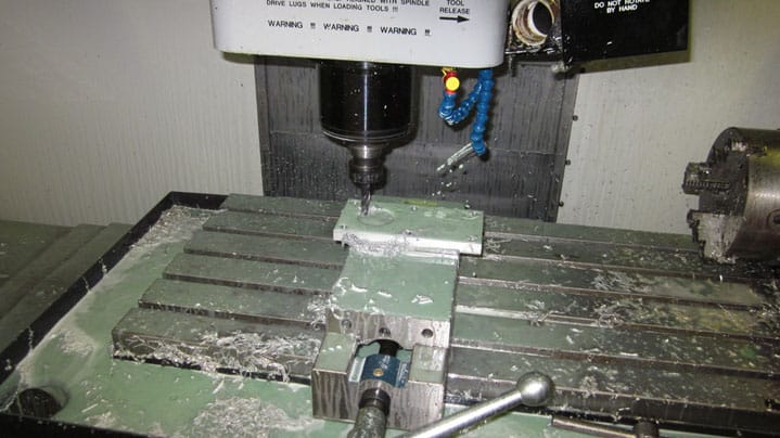 A milling machine with various components and features visible, on a cluttered workshop table with metal shavings.