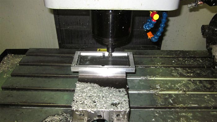 Heavy-duty milling machine with workpiece, shavings, and chips on a black and white base with spindle and metalwork clamps.