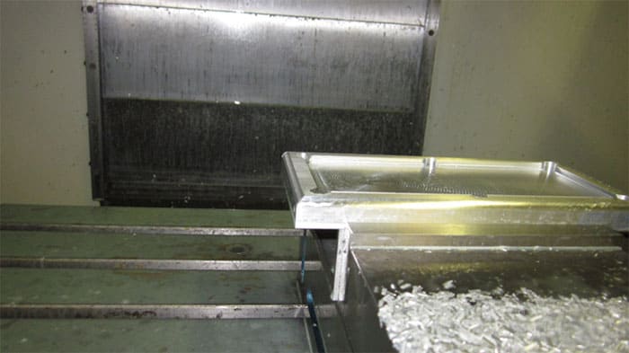 Stainless steel trough filled with water and ice, positioned in front of a large metal door.