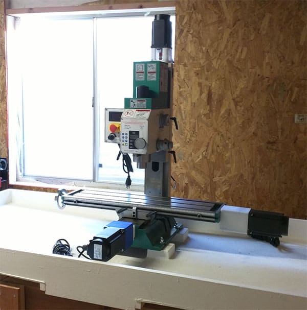 Large metalworking machine with long arm and controls in a workshop or garage setting.