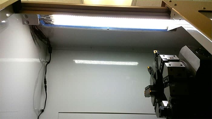 Fluorescent light fixture in a brightly lit enclosed space with white walls and ceiling.