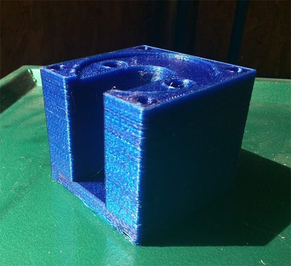 Blue 3D printed motor mount with cylindrical hole on green surface.