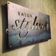 A rectangular metal sign with cursive text "SALON Stylish" in gold and faded background.