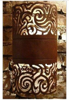 A cylindrical metal wall sconce with an intricate cutout design featuring a stylized wave pattern.
