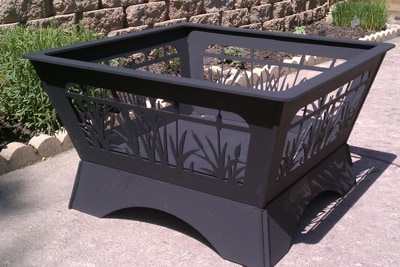 A black outdoor fire pit with decorative cutout design and lush green surroundings.