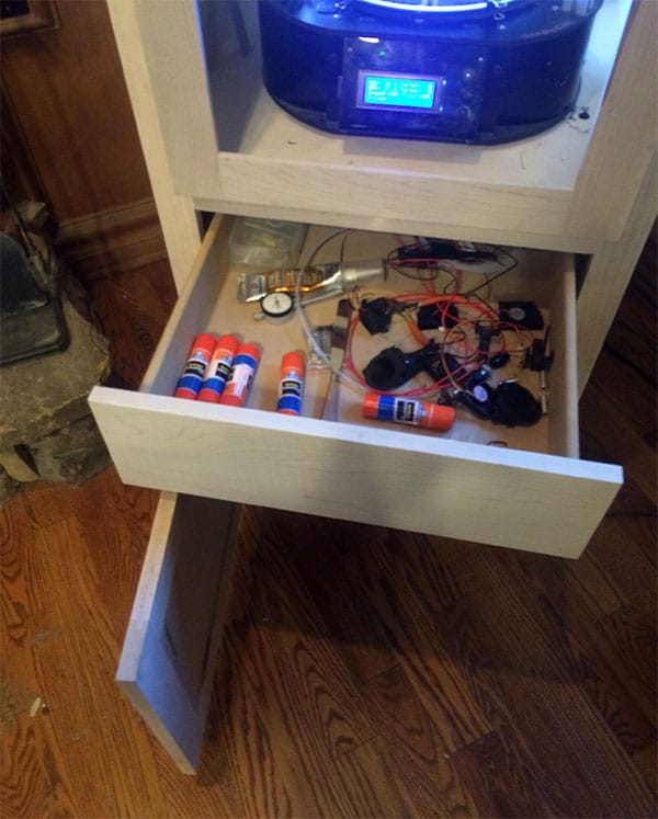 A wooden cabinet with open drawer containing various tools and components.