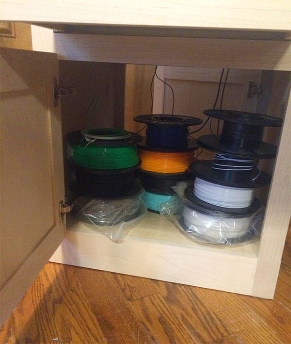 Wooden cabinet with open door showing neatly organized storage space with colored wire or cable.