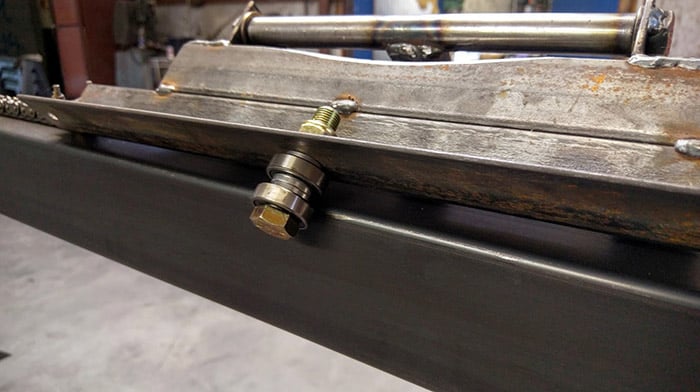 Steel object with two bolts and nuts on a gray concrete floor.