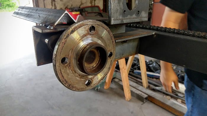 Rusty wheel hub assembly with nut, washer, and chain, on a workbench or floor.