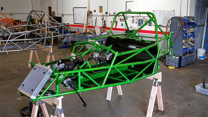 Vibrant green metal frame with complex tubing on sawhorses in a workshop setting.