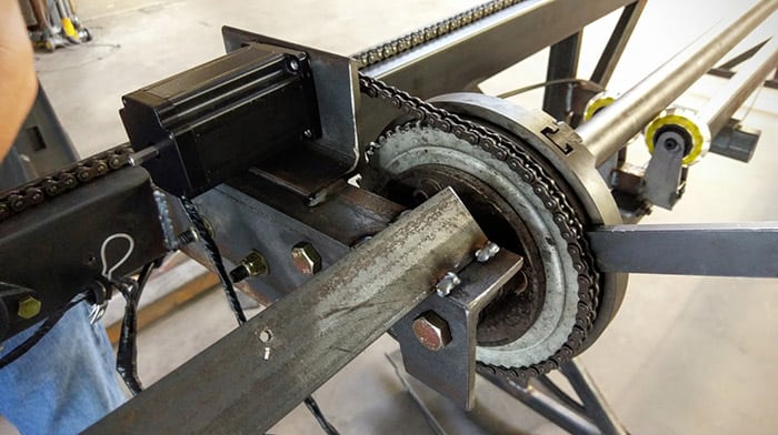 Black metal chain wrapped around a gray gear on a metal frame with a silver rod.