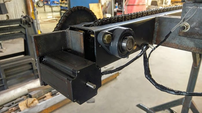 Black metal chain drive mechanism with sprocket and cable attachment.