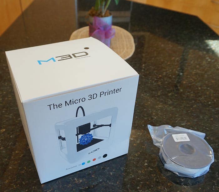 A white box for 'The Micro 3D Printer' by M30 on a dark countertop with a plant in the background.