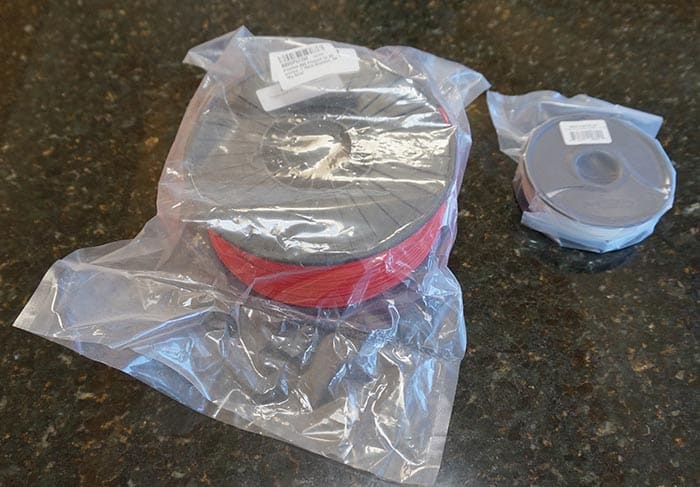 Red wire spool in clear plastic bag on dark surface.