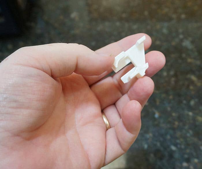 A hand holding a small white plastic object with a central hole and two prongs.