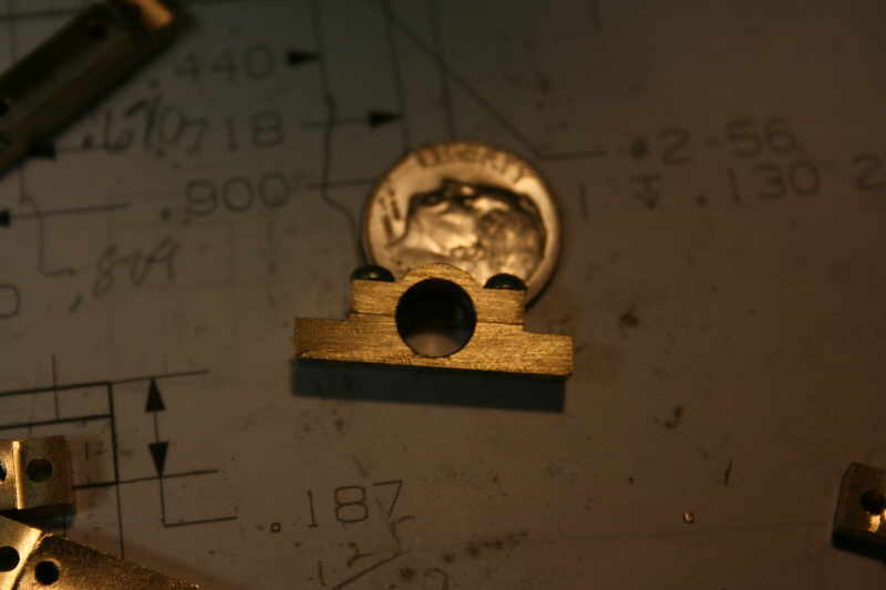 Brass part with central hole on white surface with handwritten notes and diagrams.